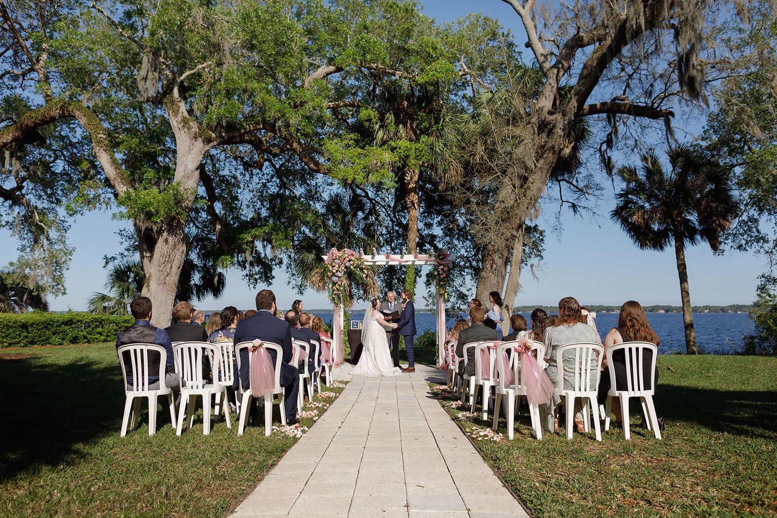 Outdoor wedding ceremony by a lake with chairs and floral arch.