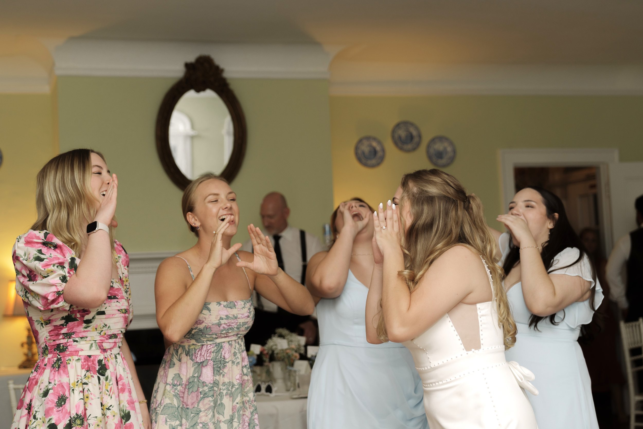 Five women in dresses laughing and clapping at a celebration.